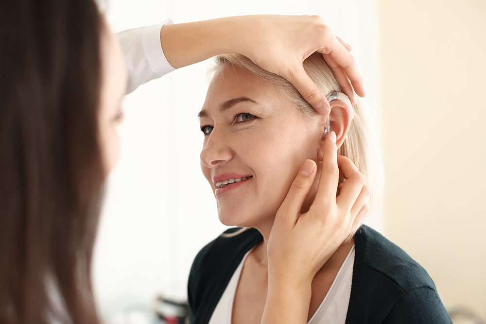 otolaryngologist,putting,hearing,aid,in,woman's,ear,on,light,background
